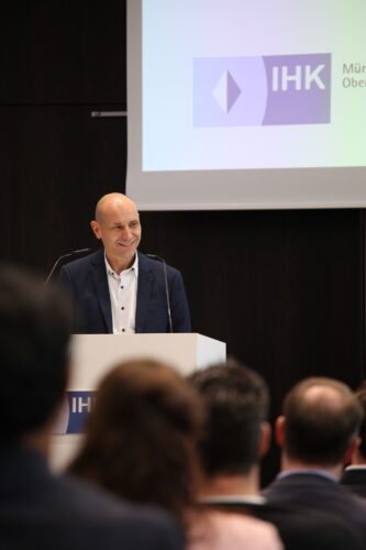 Armin Barbalata standing at the podium, welcoming the participants. A presentation can be seen on a screen in the background