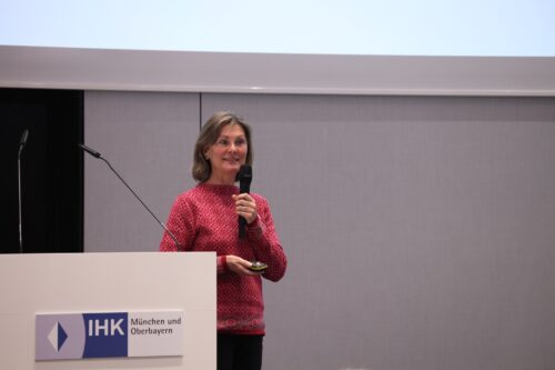 Manuela Seeholzer holding a microphone in her hand and standing in front of a screen on which her presentation can be seen